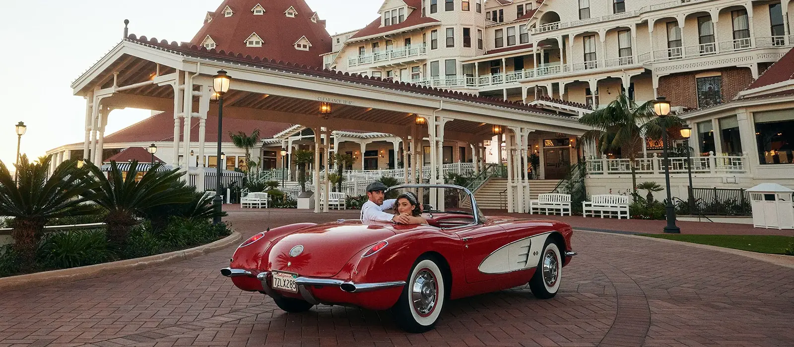Couple driving a classic red convertible in front of the historic Hotel del Coronado in California.